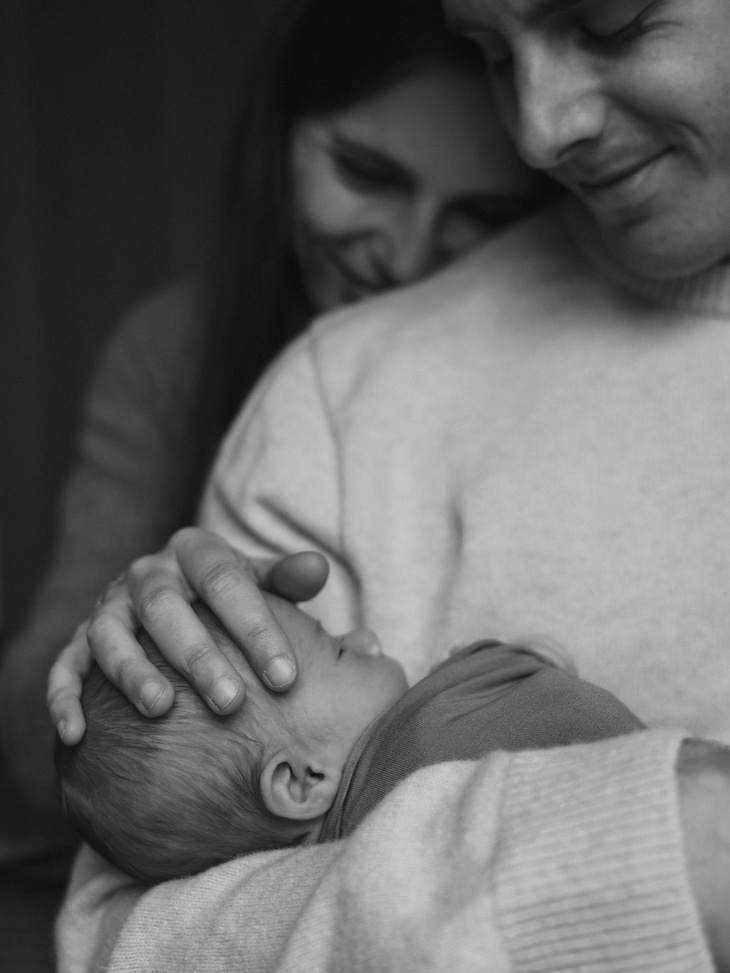 Photo de famille, nouveau-né dans les bras de papa et maman juste derrière.