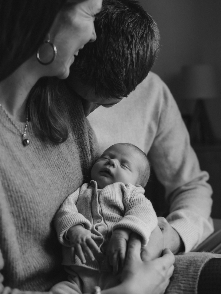 Photo nouveau-né dans les bras de ses parents qui sourient.